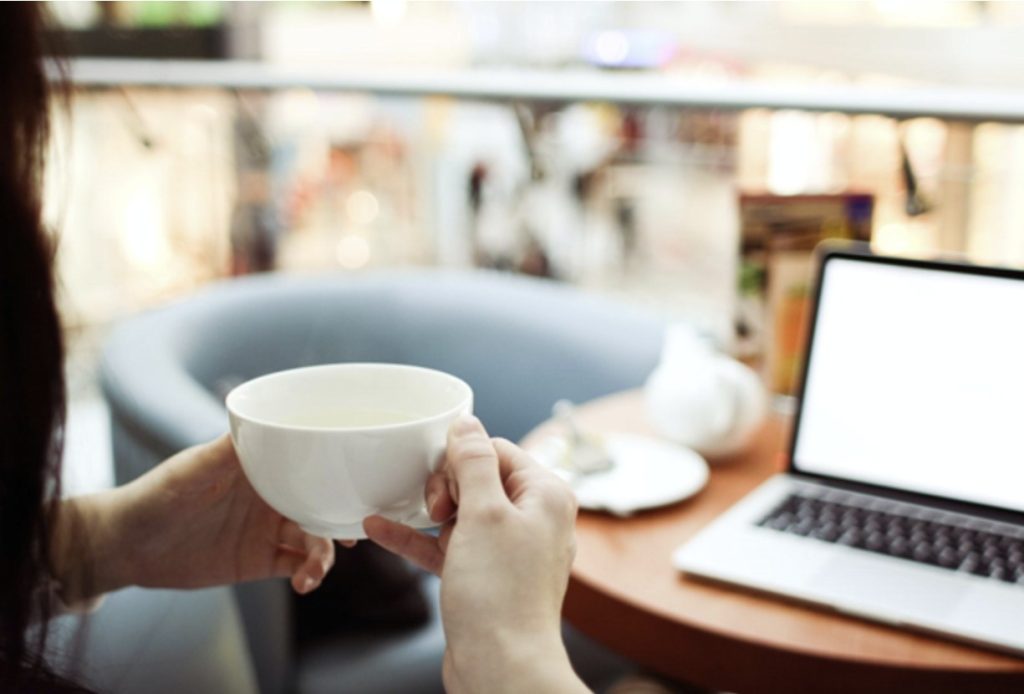 a woman holding a coffee mug sitting at a table with a laptop